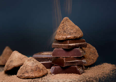 Chocolate candy truffle and chocolate pieces and flying cocoa powder on a dark backgroundの写真素材