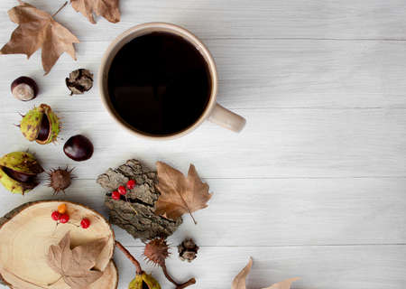 Autumn composition. Autumn layout on a light wooden background. Chestnuts, yellow dry leaves and a cup of coffee.の写真素材