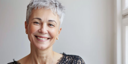 A smiling senior woman with short gray hair, wearing a scarf, looking at the camera with a warm expression. High quality photoの素材