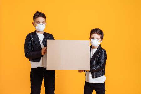 COVID-19. Coronavirus. Trendy fashionable young guys hold sign with place for text, wearing protective face masks trying to protect from virus epidemic over yellow background in photostudioの写真素材