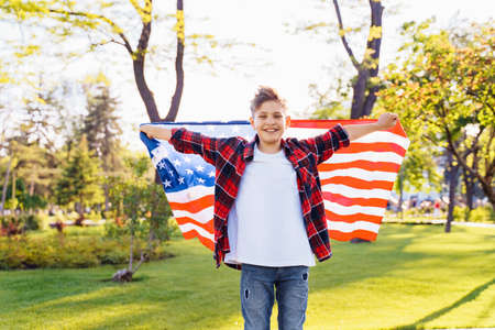 A young boy standing in the park with the USA flag of America and smiling.の写真素材