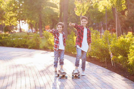 Two pretty brothers of Caucasian nationality standing in the sunny summer park on skateboards....