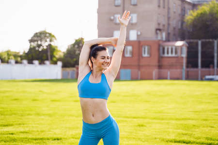 Active, slim caucasian girl 25 years old with a beautiful body exercising on field of green grass at a sports stadium. Morning begins actively and with a smile. Exercise adds energy for all day.の写真素材