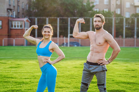 Exercises in pairs. Attractive athletes girl and guy demonstrating pumped up body. Guy is standing with a naked torso, girl is wearing a blue top and leggings. Showing muscles on the arms.の写真素材