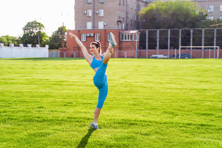 Man standing on his hands upside down and woman holding him. Strong, muscular extreme sportsmen. Young athletes of Caucasian nationality standing on the football field and doing physical exercises.の写真素材