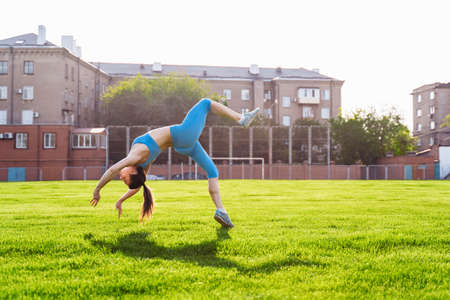 Man standing on his hands upside down and woman holding him. Strong, muscular extreme sportsmen. Young athletes of Caucasian nationality standing on the football field and doing physical exercises.の写真素材