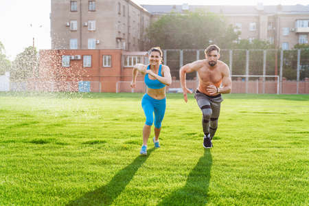Man standing on his hands upside down and woman holding him. Strong, muscular extreme sportsmen. Young athletes of Caucasian nationality standing on the football field and doing physical exercises.の写真素材