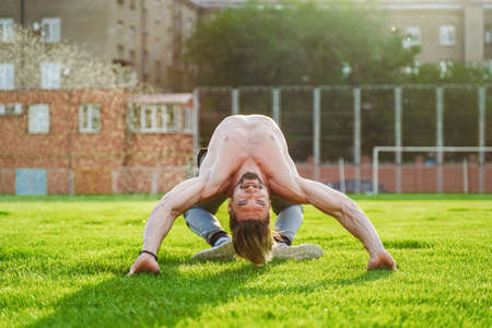 Like a spider or bug. Attractive male acrobat performing bridge sport exercise. Showing the wonders of flexibility. Training in a large grass-covered city stadium.の写真素材