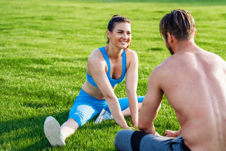 Man standing on his hands upside down and woman holding him. Strong, muscular extreme sportsmen. Young athletes of Caucasian nationality standing on the football field and doing physical exercises.の写真素材