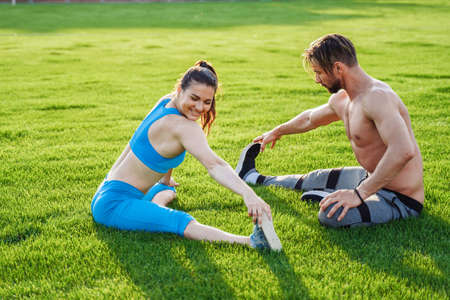 Man standing on his hands upside down and woman holding him. Strong, muscular extreme sportsmen. Young athletes of Caucasian nationality standing on the football field and doing physical exercises.の写真素材