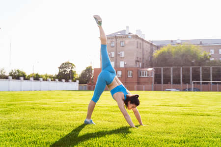 Incredibly beautiful, athletic girl does exercises at the sports city stadium on a warm summer evening. Making a stand upside down on hands.の写真素材