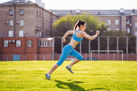 Incredibly beautiful, athletic girl does exercises at the sports city stadium on a warm summer evening. Making a stand upside down on hands.の写真素材