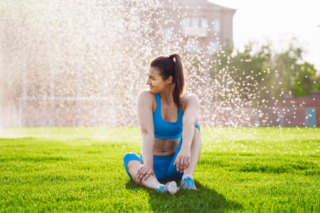 Beautiful, attractive, charming brunette having fun at the football stadium on a warm summer evening. Wrinkles from water from the field irrigation system, cooling under drops of water.の写真素材