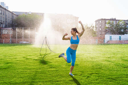 Beautiful, attractive, charming brunette having fun at the football stadium on a warm summer evening. Wrinkles from water from the field irrigation system, cooling under drops of water.の写真素材