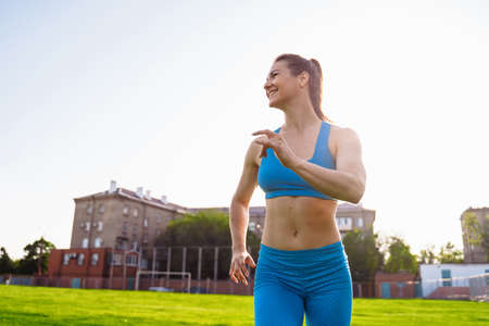Athletic muscled young woman in a sports wearing doing fitness exercises. Fitness woman posing at the stadium. Healthy athletic lifestyle.の写真素材