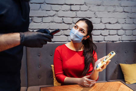 Social distancing during the  pandemic. A restaurant visitor wearing a face mask making an order through the menu on the phone. Online menus help prevent the spread of infection.の写真素材
