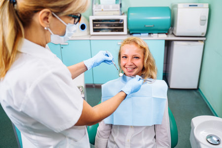 Beautiful young girl at the dentist appointment. An experienced dentist checking the health of patients teeth in a modern dental office. Portrait of smiling girl on a dental chair in dentistry.の写真素材