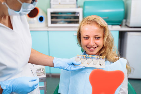 After dental treatment. The patient looks at healthy, snow-white, radiant smile after dental procedures. Tooth-shaped mirror. Satisfied with the result of going to the clinic.の写真素材