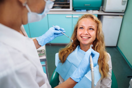 Cute european girl at the dentist's appointment. Close-up of a dentist's hands with medical instruments. Drill and tweezers in action. Selective focus. Dental care, taking care of teeth.の写真素材