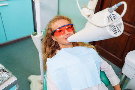 Teeth whitening. A patient in protective glasses from the rays in the chair at the dentist. Preventive examination of the oral cavity. Installing the mouth spacer. At the dentist appointment.の写真素材