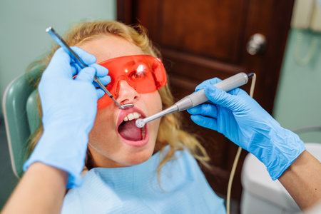 Charming girl patient sitting at the reception in the dental chair. She is wearing red safety glasses that protect against harmful radiation. Dental procedures in a modern, equipped office.の写真素材