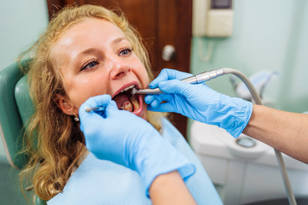 Dental treatment process. Drilling out problem areas of tooth and installing filling. Beautiful European patient sits in dentist's chair with an open mouth. Dentist holds medical instruments in hands.の写真素材