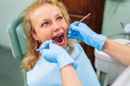 Cute european girl at the dentist's appointment. Close-up of a dentist's hands with medical instruments. Drill and tweezers in action. Selective focus. Dental care, taking care of teeth.の写真素材