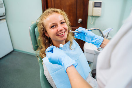 Dental treatment process. Drilling out problem areas of tooth and installing filling. Beautiful European patient sits in dentist's chair with an open mouth. Dentist holds medical instruments in hands.の写真素材