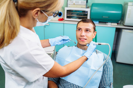 Dental inspection is being given to Beautiful man surrounded by dentist and his assistant. Woman dentist in the dental office talking to the patient and getting ready for treatment.の写真素材