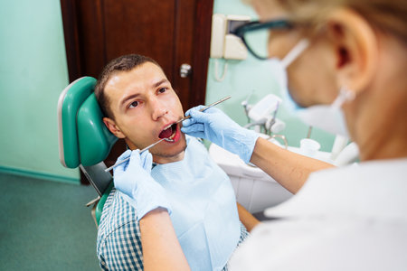 Patient with open mouth in dental clinic. Preparation for dental treatment. Using cotton wool to collect saliva, bor machine, dental mirror, tweezers and other devices. Timely treatment is important.の写真素材
