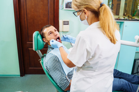 Patient with open mouth in dental clinic. Preparation for dental treatment. Using cotton wool to collect saliva, bor machine, dental mirror, tweezers and other devices. Timely treatment is important.の写真素材