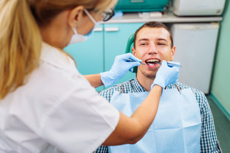 Patient with open mouth in dental clinic. Preparation for dental treatment. Using cotton wool to collect saliva, bor machine, dental mirror, tweezers and other devices. Timely treatment is important.の写真素材