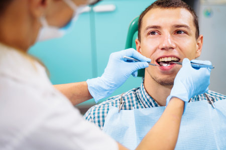 Patient with open mouth in dental clinic. Preparation for dental treatment. Using cotton wool to collect saliva, bor machine, dental mirror, tweezers and other devices. Timely treatment is important.の写真素材