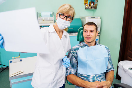 Mature woman dentist looks at teeth x-rays. Discussion of issues. Cropped shot of professional dentist showing jaw and teeth with x-rays to patient using digital technology. Health issues.の写真素材