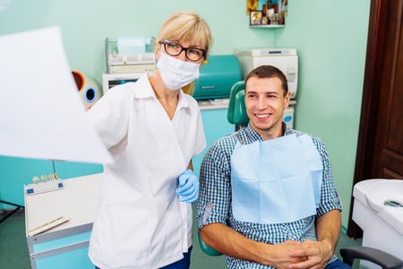Mature woman dentist looks at teeth x-rays. Discussion of issues. Cropped shot of professional dentist showing jaw and teeth with x-rays to patient using digital technology. Health issues.の写真素材