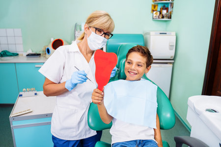 After dental treatment. The patient looks at healthy, snow-white, radiant smile after dental procedures. Tooth-shaped mirror. Satisfied with the result of going to the clinic.の写真素材