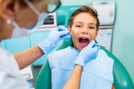 A small patient with an open mouth at a dentist appointment in a modern clinic. Hands of unrecognizable pediatric dentist doing examination procedure for smiling cute boy in hospital.の写真素材