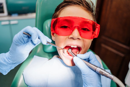 Spot illumination with the light of lamp of a tooth with caries. Young boy at the dentist's office at the examination. Dentist checking teeth of patients in dental chair under bright light in clinic.の写真素材