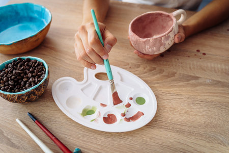 Hand dipping paintbrush into palette on wooden table. Finishing manufacturing procces of clay pottery production. Exclusive handmade products turquoise and royal blue bowlsの写真素材