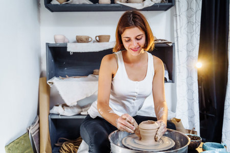 Art workshop, pottery, ceramics. Young master woman working with her hands with a potter's wheel. Carefully, diligently sculpting a jug, Cup, mug from raw clay.の写真素材