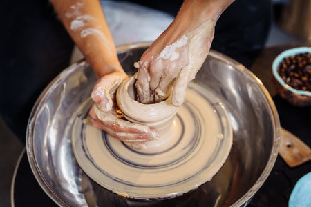 Close-up of the hands of a woman ceramist working with a potter's wheel in a cozy, bright workshop. A young experienced woman skillfully makes a mug, vase or plate. Creative people, pottery workshop.の写真素材