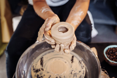 Close-up of the hands of a woman ceramist working with a potter's wheel in a cozy, bright workshop. A young experienced woman skillfully makes a mug, vase or plate. Creative people, pottery workshop.の写真素材