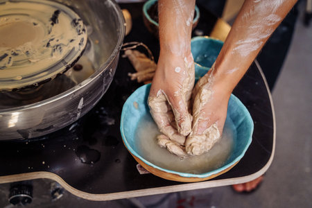 Professional woman potter washing her hands from clay in a hand made ceramic plate. Finished work on the next item vase, cup, mug and is preparing to clean the workshop room.の写真素材