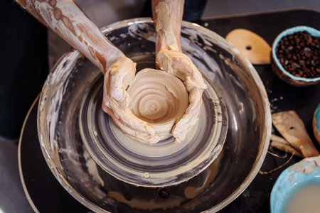Close-up of the hands of a woman ceramist working with a potter's wheel in a cozy, bright workshop. A young experienced woman skillfully makes a mug, vase or plate. Creative people, pottery workshop.の写真素材