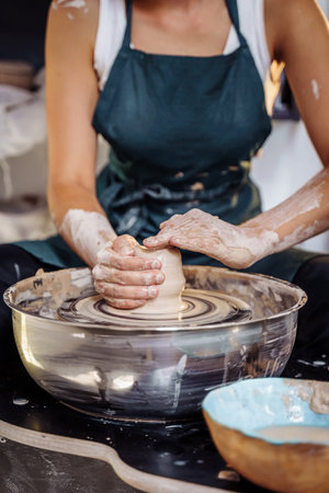 With professional hand movements, a female potter prepares a piece of clay on a potter's wheel, kneads the clay and rolls it out to make a bowl, vase, jug, plate. Pottery studio. Young professional.の写真素材