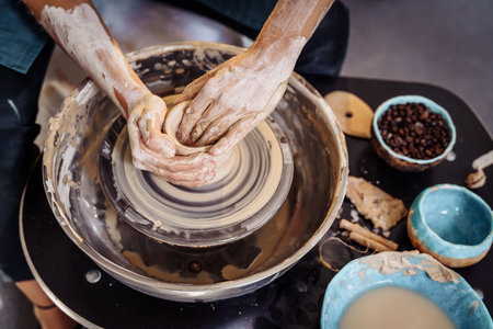 Close-up of the hands of a woman ceramist working with a potter's wheel in a cozy, bright workshop. A young experienced woman skillfully makes a mug, vase or plate. Creative people, pottery workshop.の写真素材