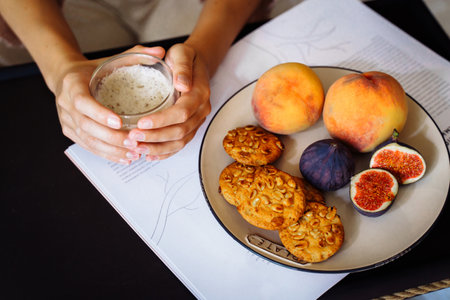 Efficient young millennial attractive woman sitting on a bed in the morning. Hand holding a cup of coffee and eating cookies. Coffee morning concept. Pleasant time during calm morning.の写真素材