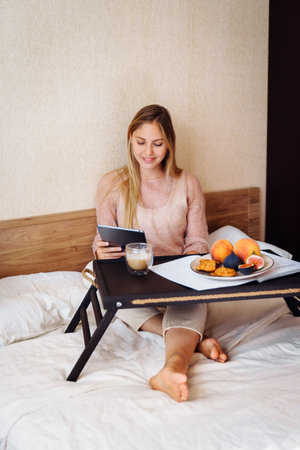 Young, pretty, attractive, charming girl blonde of European appearance, is smiling widely on tablet with friends and relatives. Using video communication, friendly waving hand, looking at the screen.の写真素材