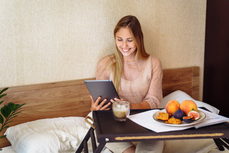 Young, pretty, attractive, charming girl blonde of European appearance, is smiling widely on tablet with friends and relatives. Using video communication, friendly waving hand, looking at the screen.の写真素材