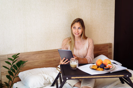 In the morning beautiful caucasian lady sitting and drinking hot tea or coffee in bed. Blond female solving work issues remotely. Cozy workplace at home. Distance learning online education and work.の写真素材
